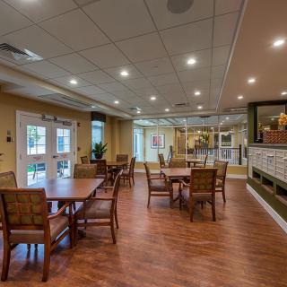 A cozy dining area with wooden floors, tables, and chairs, illuminated by ceiling lights.