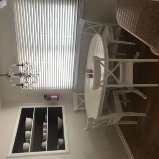 A cozy dining room with a round white table, matching chairs, a chandelier, and wall shelves displaying plates.