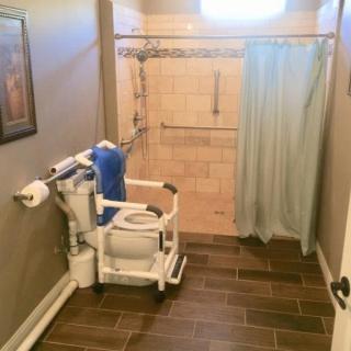 An accessible bathroom featuring a shower with a curtain and a mobility aid chair.