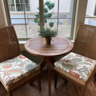 A cozy indoor seating area with a wooden table, two chairs with patterned cushions, and a small potted plant by the window.