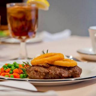 A delicious steak topped with grilled pineapple, accompanied by a side of peas and carrots, served with a glass of iced tea.