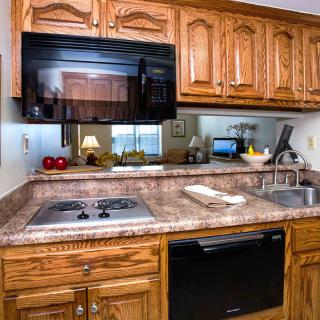 A cozy kitchen featuring wooden cabinets, a stove top, microwave, and a sink on a granite countertop.