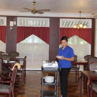 A server in a dining room setting with red curtains, pushing a cart with dishes.