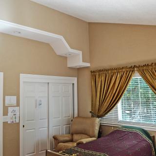 A cozy bedroom featuring a unique cat shelf above the closet, with an armchair placed near a window adorned with elegant curtains.