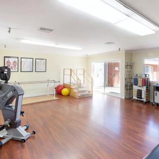 A spacious gym with exercise equipment and wooden flooring, ideal for fitness and rehabilitation activities.