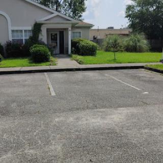 A view of a building front with an empty parking lot and well-maintained green grass.