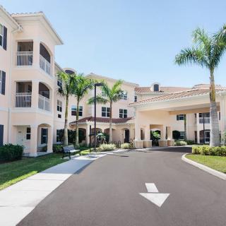 A sunny exterior view of a multi-story building with palm trees and a driveway leading to the entrance.