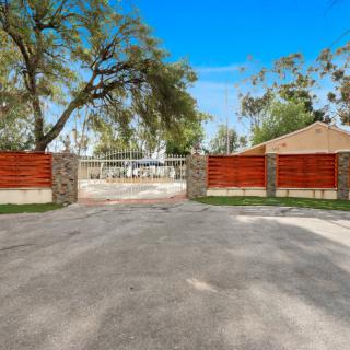A residential entrance with a red wooden gate and stone pillars, surrounded by trees.