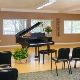 A grand piano in a music room with chairs arranged for an audience and decorative flowers nearby.