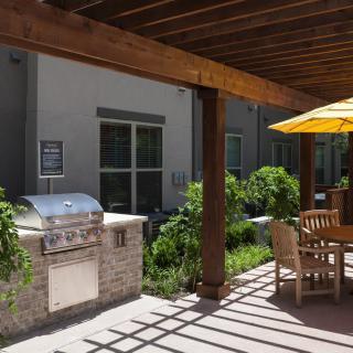 A sunny outdoor patio with a barbecue grill and dining area under a wooden pergola.