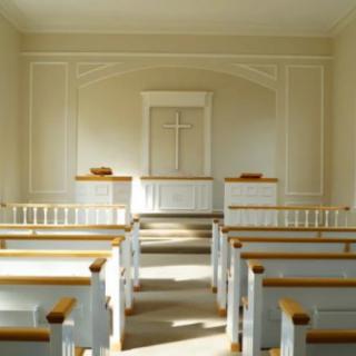 Interior view of a serene chapel with wooden pews and a central altar featuring a cross.