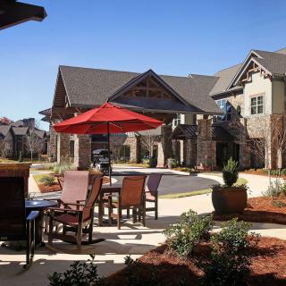 A cozy outdoor patio area with tables and chairs under a red umbrella, set against modern residential buildings.