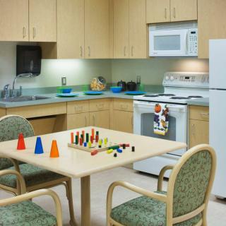 A kitchen setup with wooden cabinetry, basic appliances, and a table with chairs featuring colorful toys.