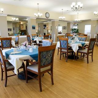 A well-lit dining room with neatly arranged tables and chairs, featuring elegant chandeliers and a wooden floor.