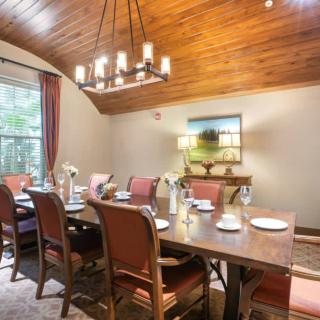 An elegantly decorated dining room with a wooden ceiling, featuring a large dining table set for guests, surrounded by upholstered chairs and illuminated by a chandelier.