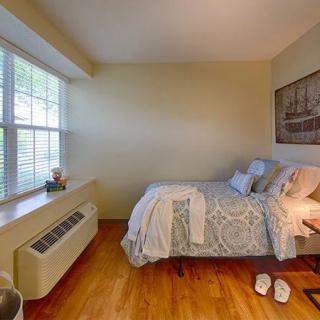 A cozy, minimalist bedroom with natural light streaming through a large window next to a neatly made bed.