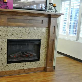 A cozy living room with a modern fireplace and wooden mantel, decorated with candles, next to a bright window.