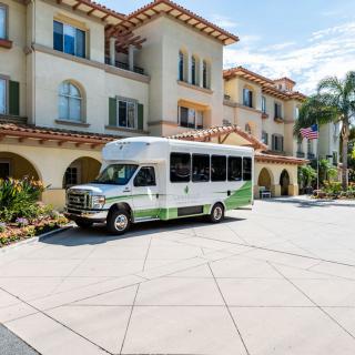A shuttle bus parked in front of a large, multi-story building with palm trees nearby.