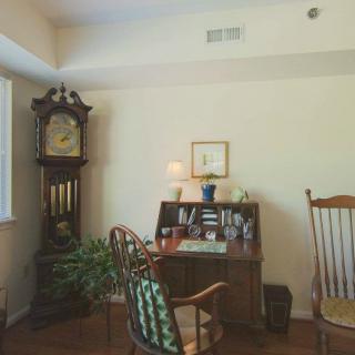 A cozy study room with a grandfather clock, wooden desk, and rocking chair.