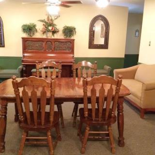 A cozy living room featuring a wooden dining table with chairs, a piano, and a comfortable couch.