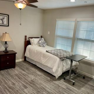 A cozy bedroom with a single bed, nightstand, and overbed table, illuminated by a ceiling fan light.