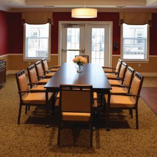 A well-lit dining room featuring a long table and chairs, with windows allowing natural light to enter.
