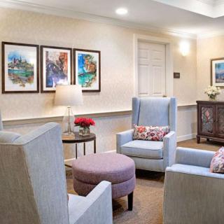 A cozy living room with comfortable armchairs, artwork on the walls, and a lamp beside a coffee table.