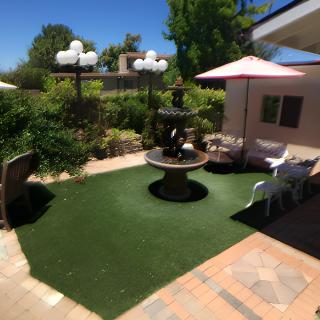 A sunny garden with a central fountain surrounded by artificial grass and patio furniture.