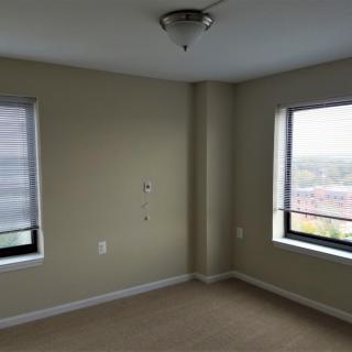 A bright, empty room with large windows and neutral-colored walls.