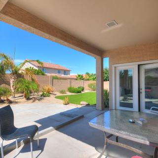 A sunny backyard with a patio and outdoor seating area, surrounded by well-maintained landscaping.