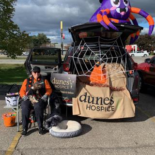 A community volunteer showcases a festive Halloween-themed trunk for a hospice charity event, complete with decorations and information about Dunes Hospice.