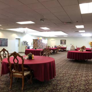 A spacious banquet hall with round tables covered in red tablecloths, set up for an event.