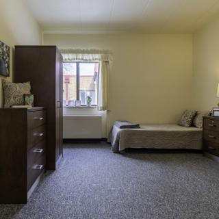 A simple bedroom with a single bed, dresser, and window.