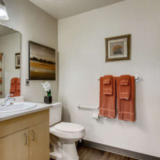 A modern bathroom with a toilet, sink, and orange towels hanging on the wall.