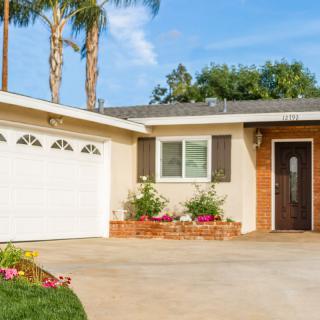 A suburban house with a garage and driveway, featuring well-maintained landscaping and palm trees.