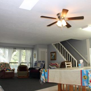 A spacious living room with a ceiling fan, staircase, and comfortable furniture.