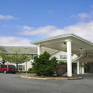 A building with a covered entrance and landscaped surroundings, including a parking area with cars.