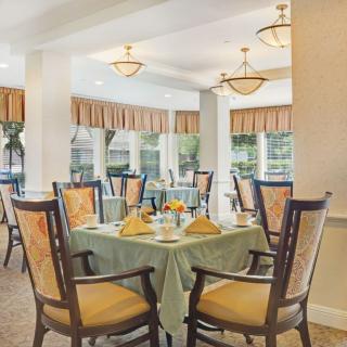 A well-lit dining room with elegantly set tables and chairs, featuring large windows that allow natural light to flood the space.