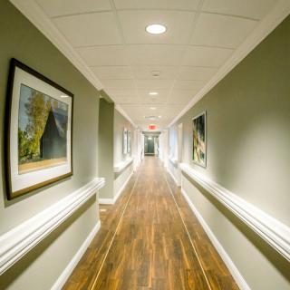 A long, well-lit corridor with wooden flooring and framed artwork on the walls.