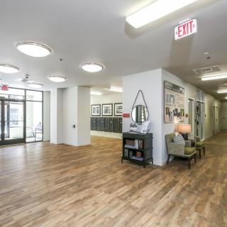 A modern lobby with a wooden floor and seating area leading to a hallway.