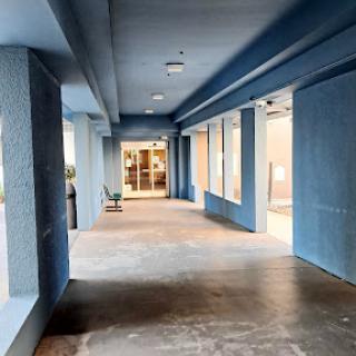 A spacious corridor featuring blue walls and large windows, leading to an entrance.