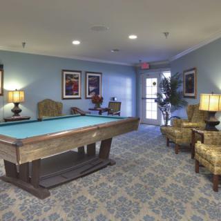 A cozy billiard room with a pool table and comfortable seating areas, decorated with lamps and artwork on the walls.