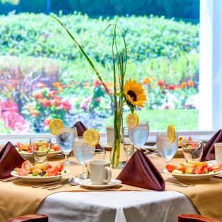 A beautifully set dining table with a sunflower centerpiece, overlooking a vibrant outdoor garden.