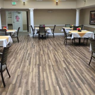 A dining area with multiple tables and chairs, featuring a wooden floor and white tablecloths.