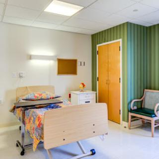 A well-appointed hospital patient room featuring a bed, chair, and warm decor.