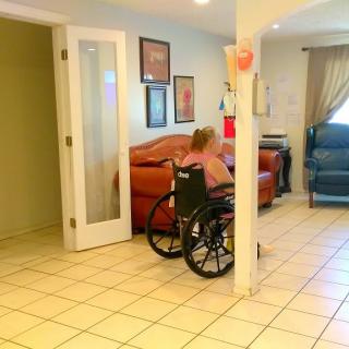 A person in a wheelchair in a living room with sofas and tile flooring.