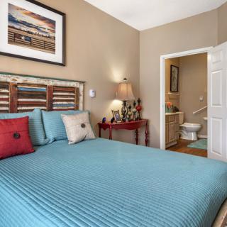 Cozy bedroom with a blue bedspread, decorative pillows, and an open doorway leading to a bathroom.
