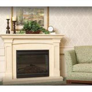 A cozy living room with a classic fireplace, adorned with a painting, candles, and a plant on the mantel, accompanied by a green couch.