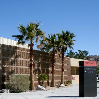 A modern building surrounded by palm trees under a clear blue sky in a desert setting.