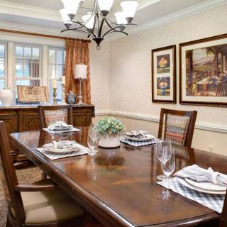 A neatly arranged dining room with a wooden table set for four, featuring a chandelier and framed artwork on the walls.